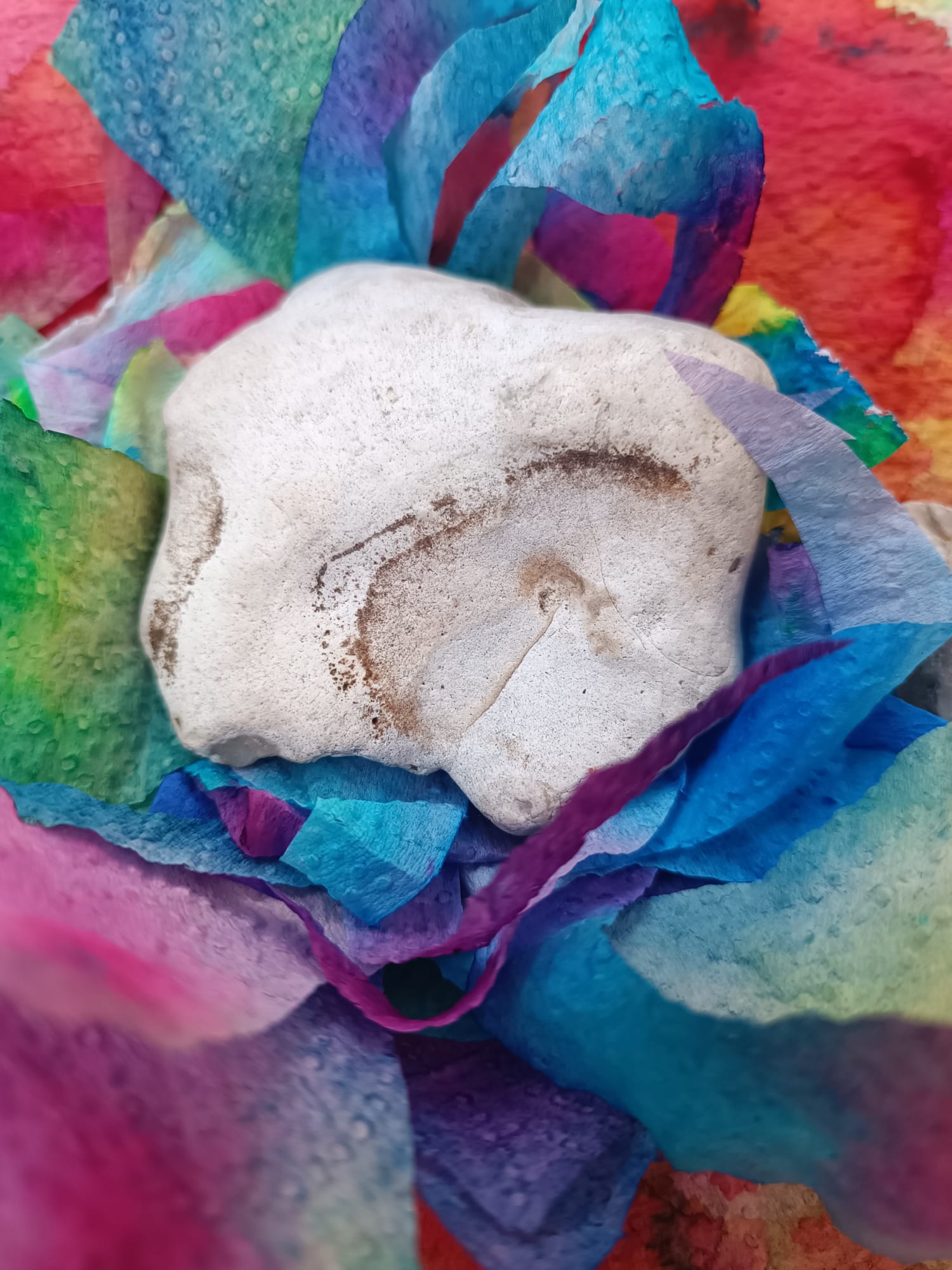 Pieza de arcilla blanca sobre papeles teñidos de colores